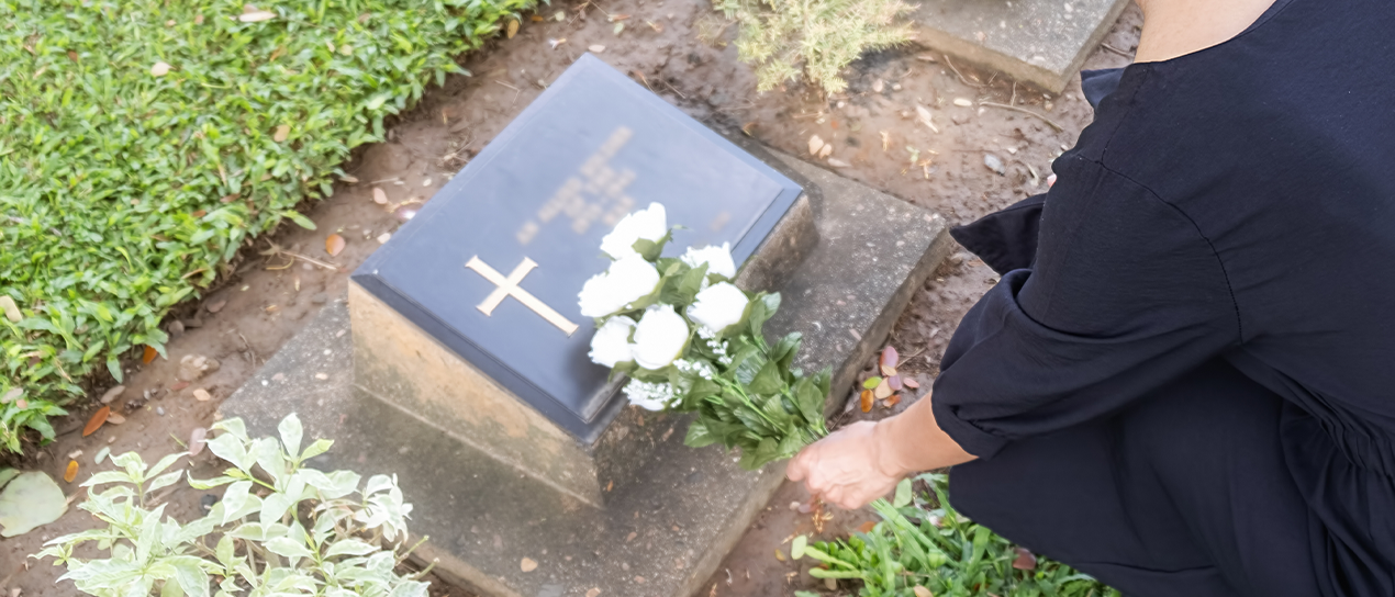 mourning young woman putting flowers on a tombstone