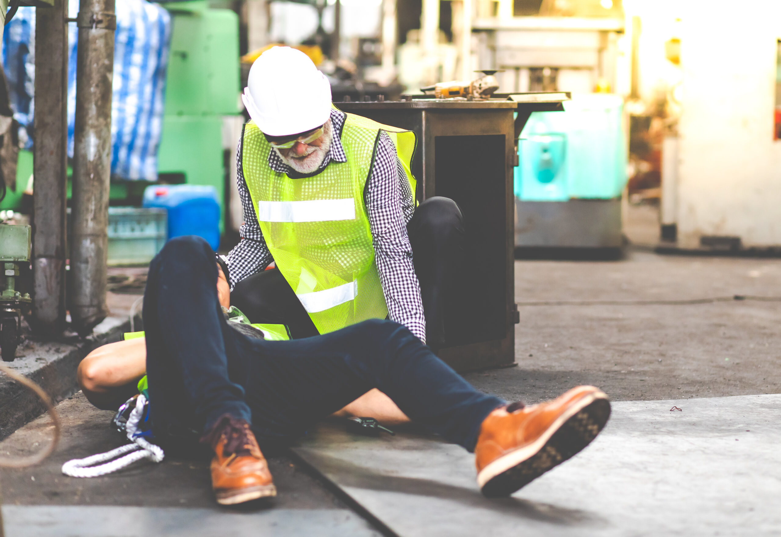 First Aid. Engineering supervisor talking on walkie talkie communication while his coworker lying unconscious at industrial factory. Professional engineering teamwork concept.