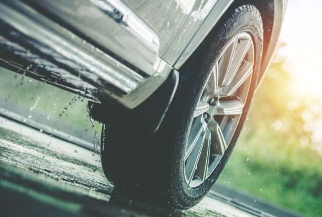 Car Driving in the Rain. Modern Rain Summer Season Tires on the Wet Pavement. Closeup Aquaplaning Photo.