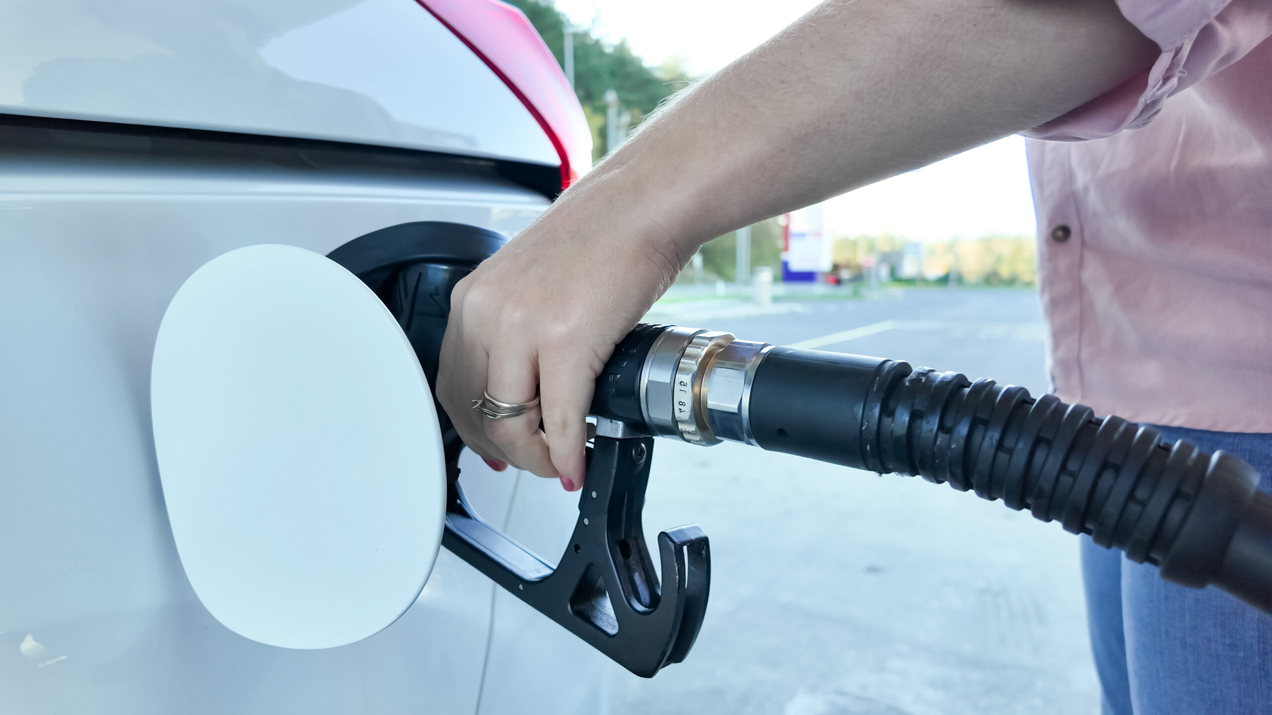 A person refuels a car at a gas station, highlighting the concept of transportation and rising fuel costs.